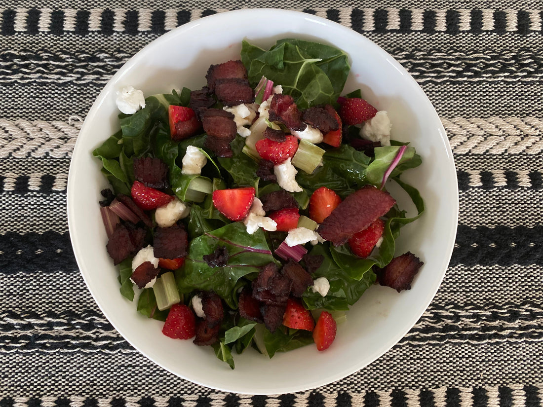 Rainbow chard with goat cheese and strawberries topped with bacon dressing for a salad in a bowl