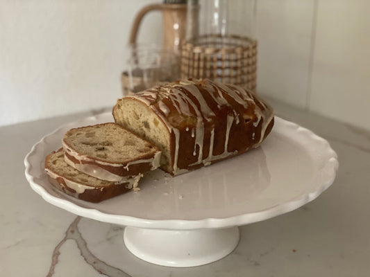 Freshly sliced rhubarb bread topped with orange glaze, served on a white scalloped edge cake stand